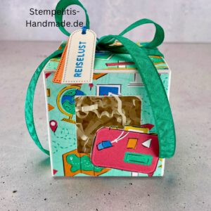 Handdekorierte Fensterschachtel mit Reisethema und grünem Band, Detailansicht des Sichtfensters mit Füllmaterial, Koffer-Motiv auf der Front der Schachtel, Oberseite mit Geschenkanhänger „Reiselust“, Seitliche Ansicht der Box mit Weltkartenmotiv, Geöffnete Box mit Blick auf das Innere, Fensterschachtel als kreative Geschenkverpackung für Reisegutscheine